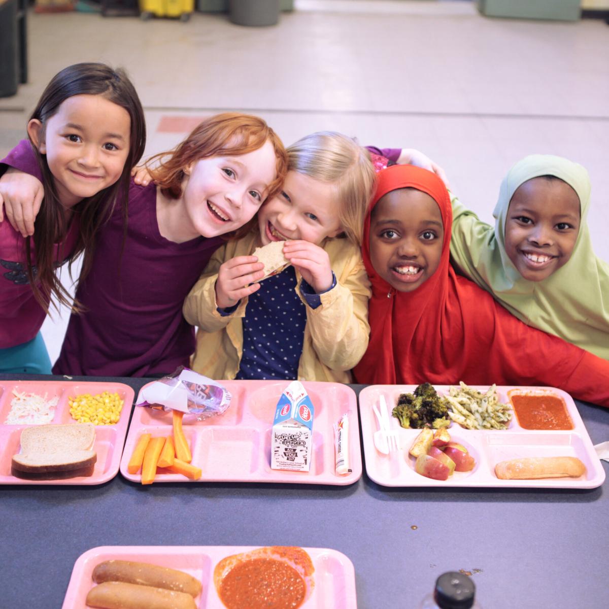 Five young students enjoy school meals in the cafeteria.