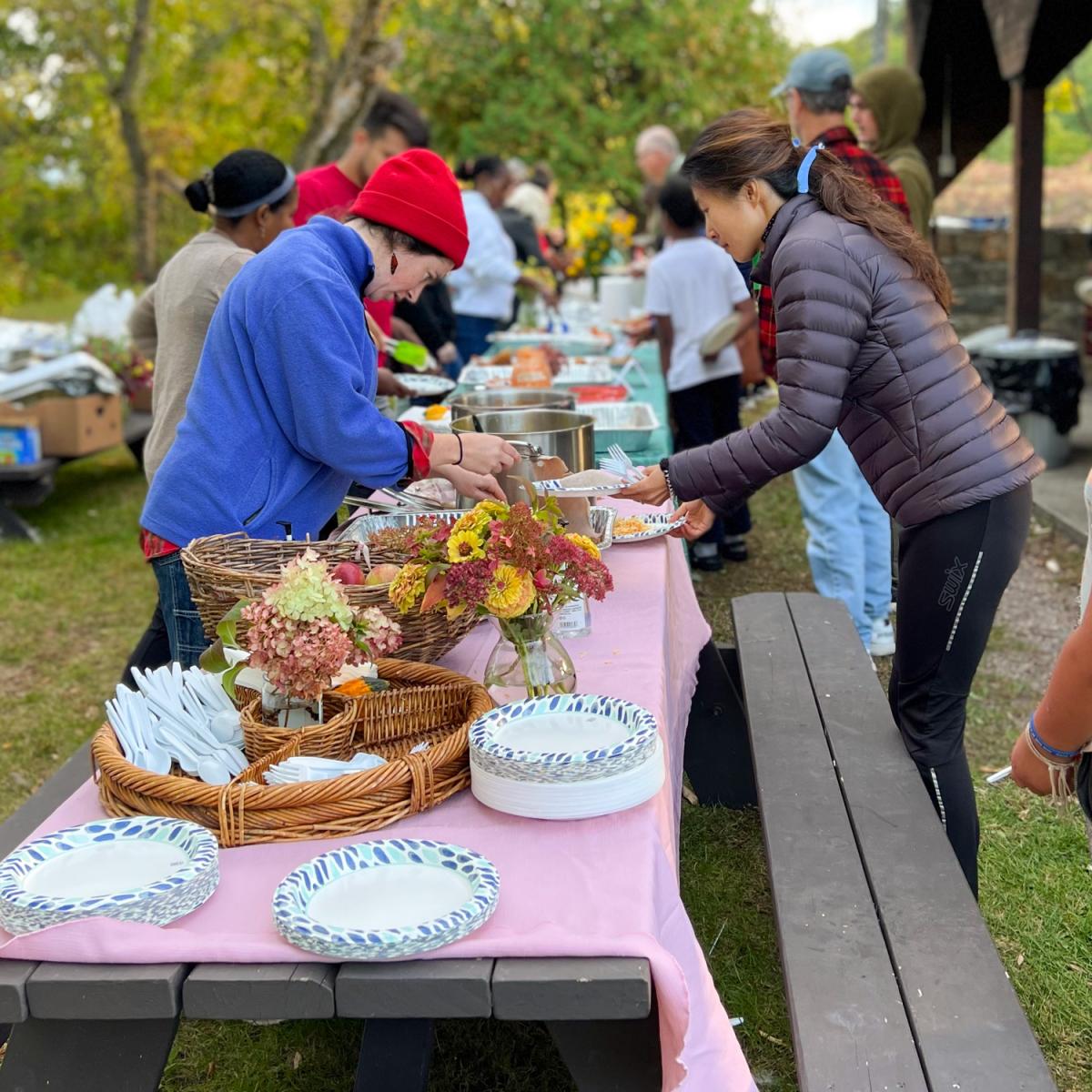 People line up at picnic tables, full of plates of food to share