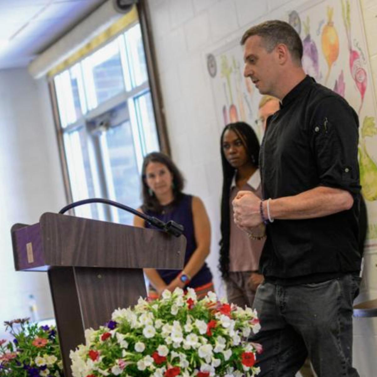 a man in a chefs coat speaks at a podium a man in a chefs coat speaks at a podium