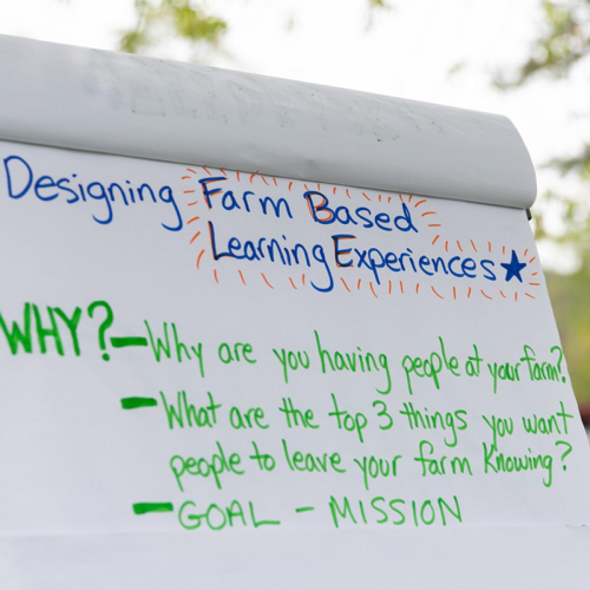 Flipchart with handwritten notes about "Designing Farm Based Learning Experiences." Questions listed include "WHY?—Why are you having people at your farm?" and "What are the top 3 things you want people to leave your farm knowing?" with headers "GOAL - MISSION". Flipchart with handwritten notes about "Designing Farm Based Learning Experiences." Questions listed include "WHY?—Why are you having people at your farm?" and "What are the top 3 things you want people to leave your farm knowing?" with headers "GOAL - MISSION".
