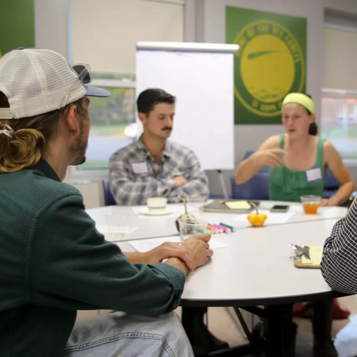 Four people sitting around a table in a meeting room, engaged in a discussion. There's a whiteboard and logo of Fairtrade in the background. Four people sitting around a table in a meeting room, engaged in a discussion. There's a whiteboard and logo of Fairtrade in the background.