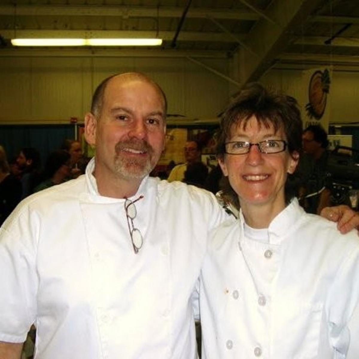 Two chefs in white uniforms smiling at the camera in a busy event setting. Two chefs in white uniforms smiling at the camera in a busy event setting.