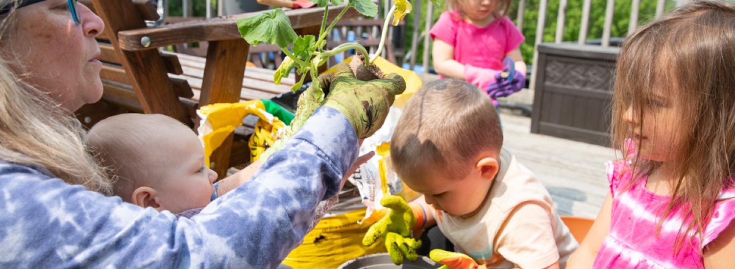 A woman plants a squash plant with a group of young children